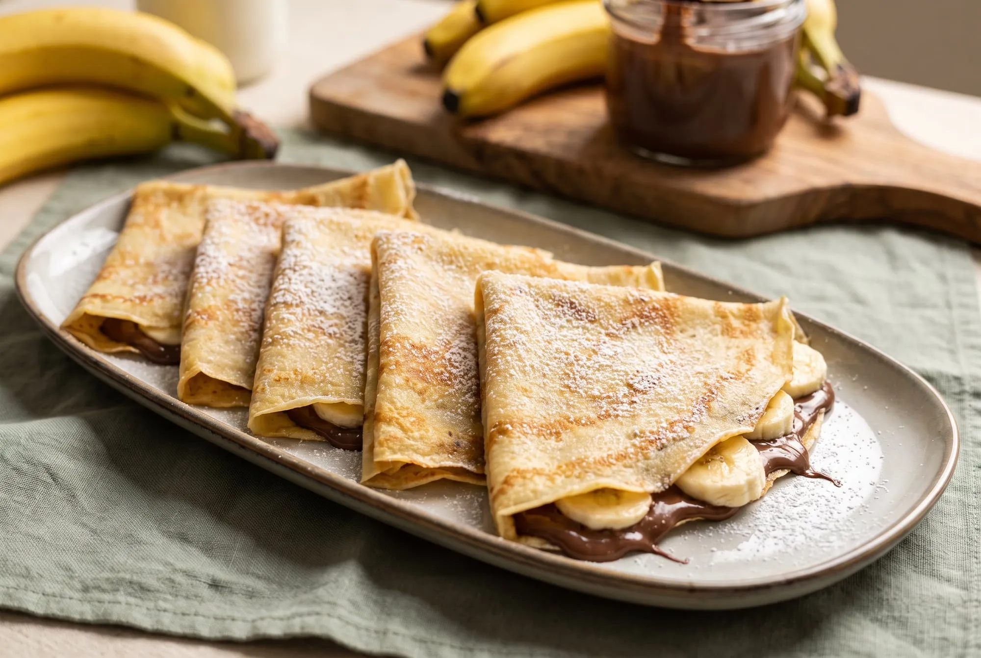 Crepes folded around chocolate-hazelnut spread and sliced bananas, dusted with powdered sugar