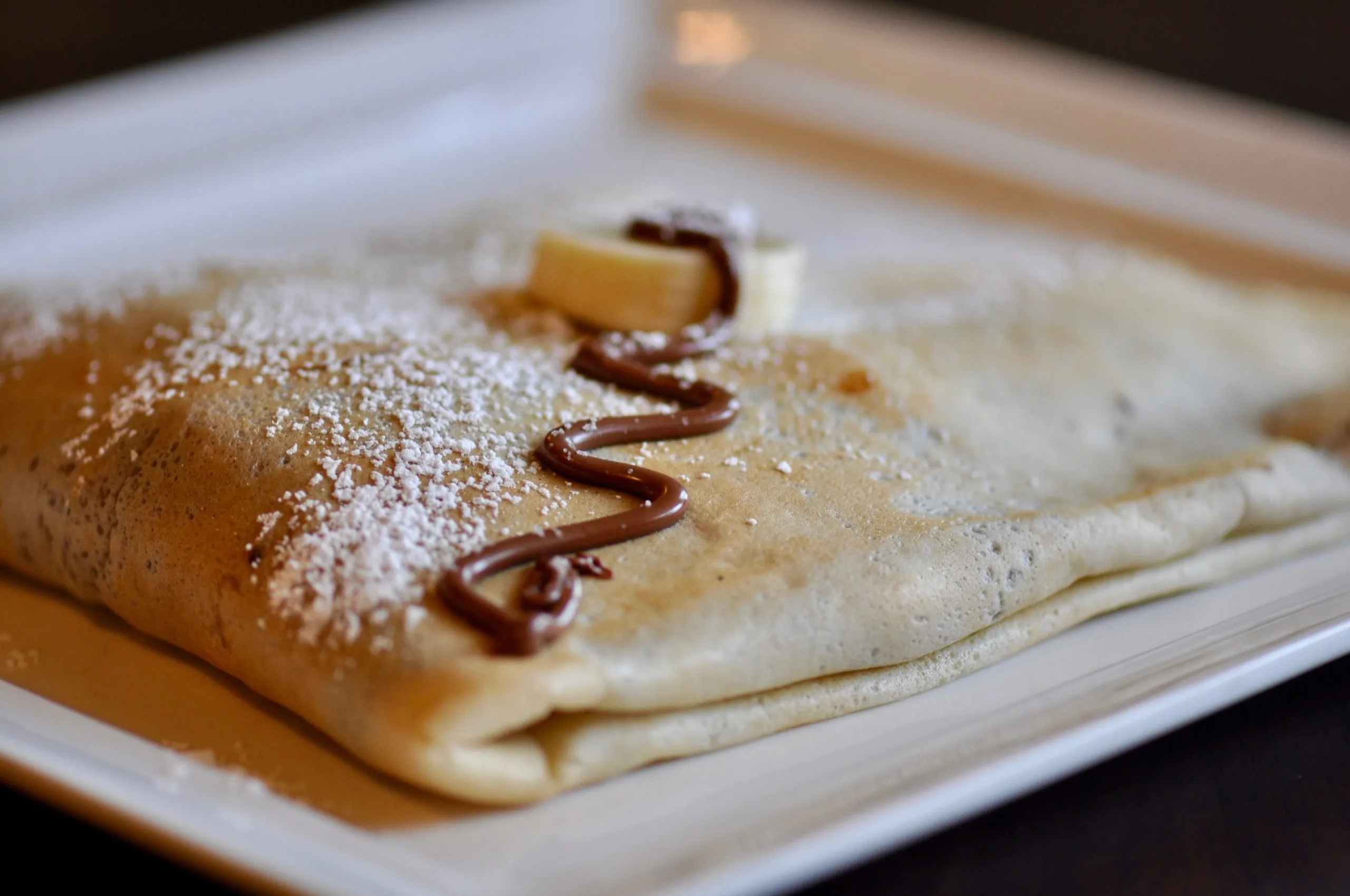 A folded crepe dusted with powdered sugar and drizzled with chocolate